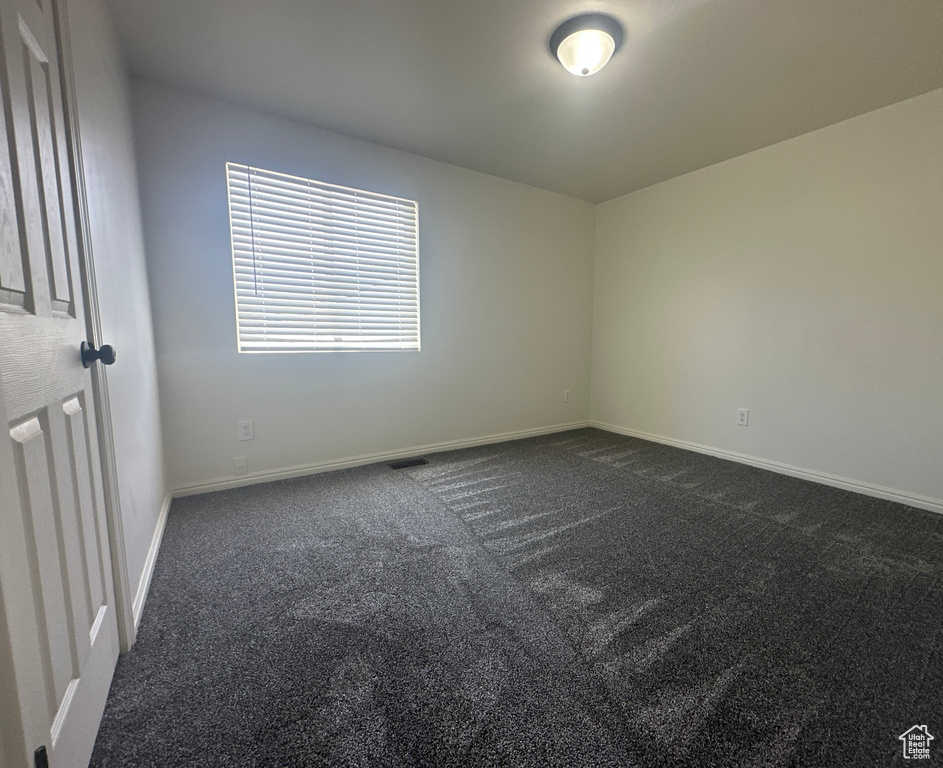 Empty room featuring dark carpet and baseboards