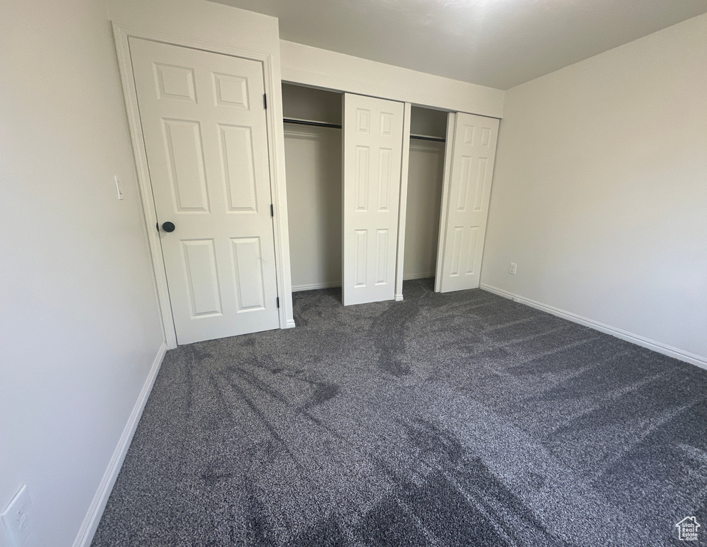 Unfurnished bedroom featuring dark carpet and a closet