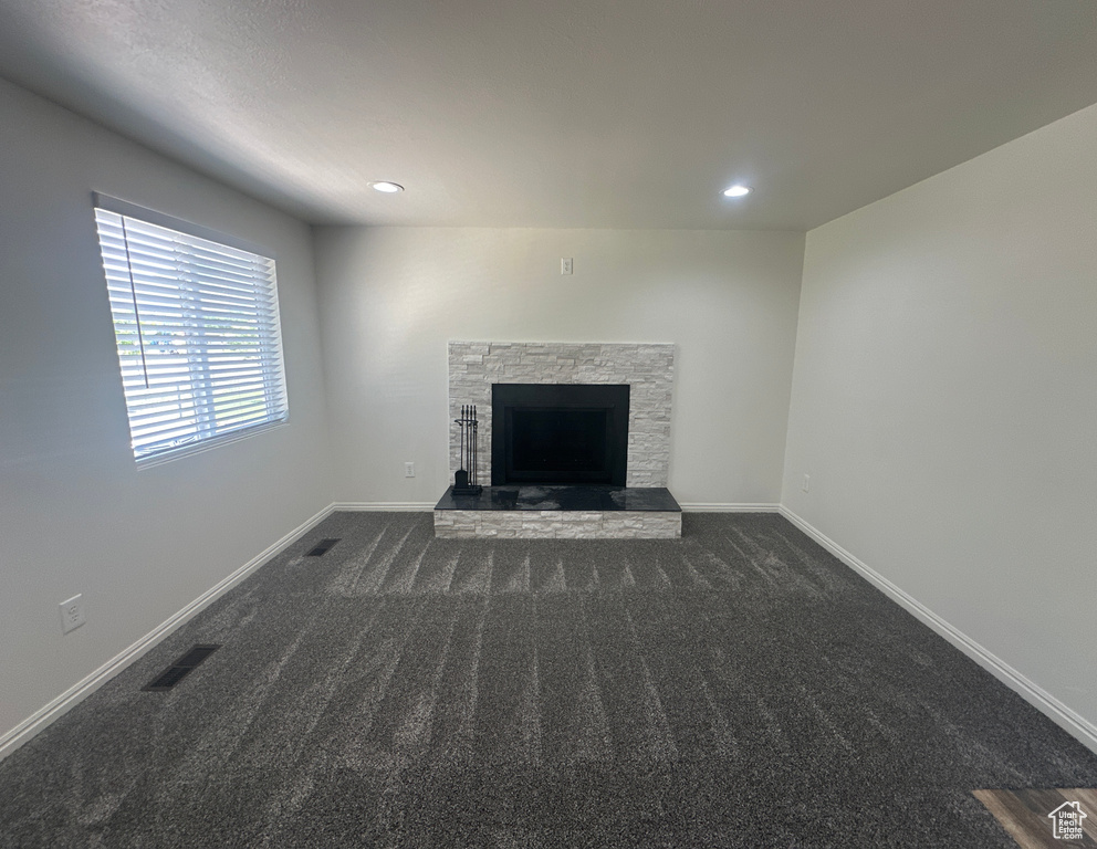 Unfurnished living room featuring dark colored carpet, a stone fireplace, and recessed lighting