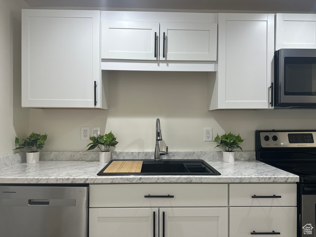 Kitchen with stainless steel appliances, white cabinets, and light stone countertops