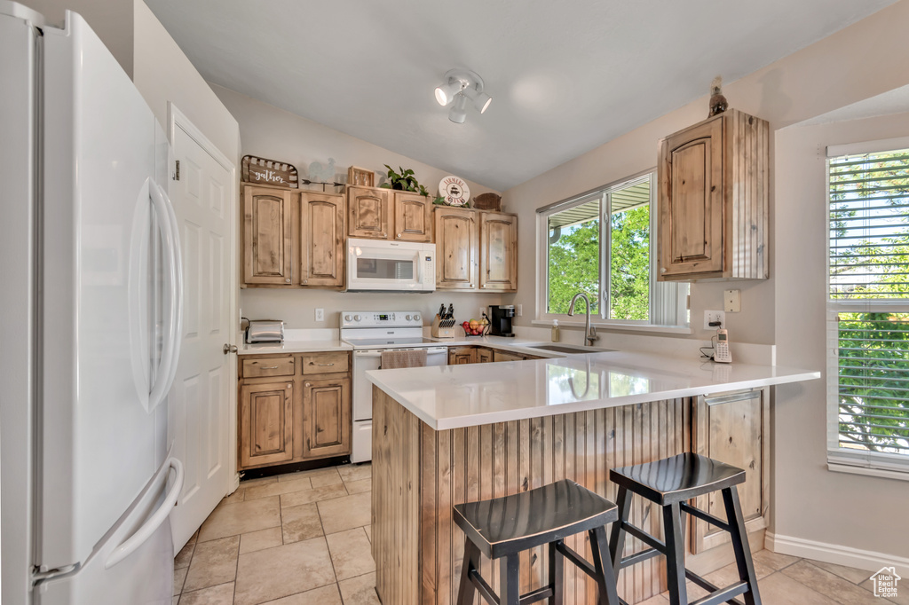 Kitchen with white appliances, a peninsula, healthy amount of natural light, and vaulted ceiling