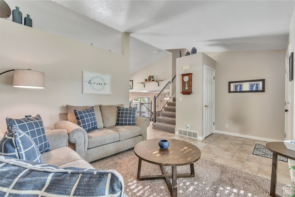 Living area featuring stairs, stone tile flooring, and high vaulted ceiling