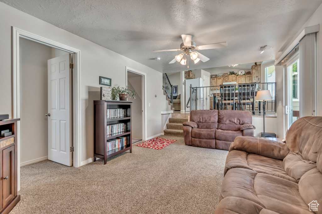 Living area featuring light carpet, a ceiling fan, stairway, and a textured ceiling