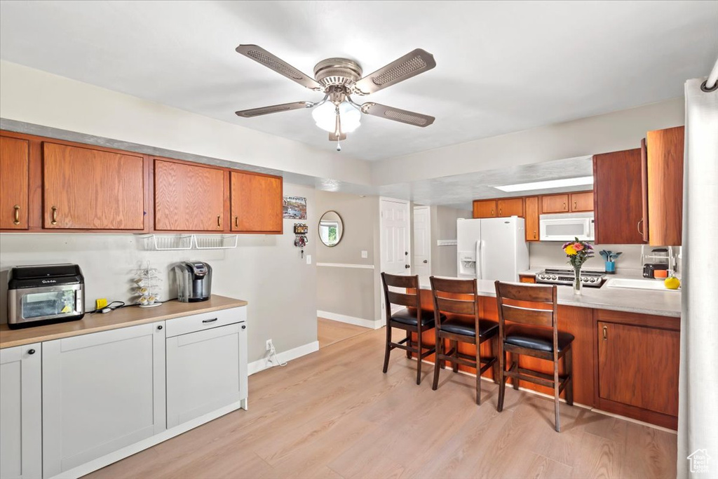 Kitchen featuring white appliances, ceiling fan, light countertops, a kitchen breakfast bar, and brown cabinetry