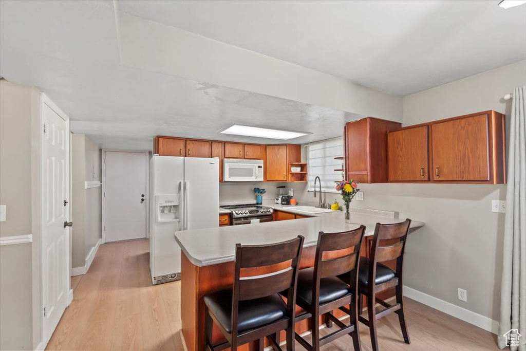 Kitchen featuring white appliances, a peninsula, light wood-style flooring, light countertops, and brown cabinetry