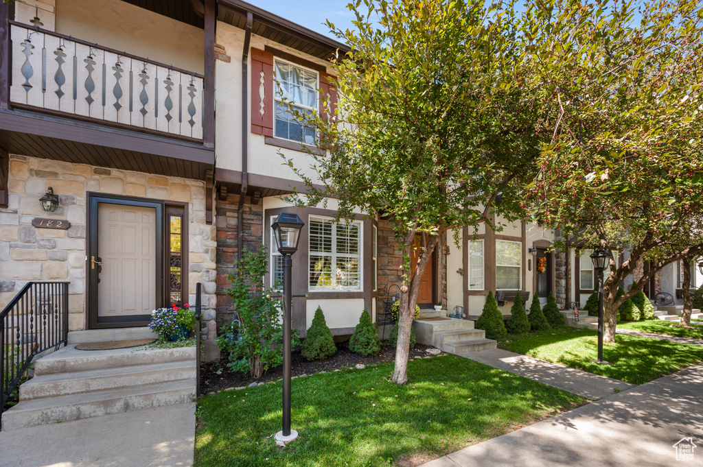 Multi unit property featuring stone siding, a balcony, a front lawn, and stucco siding