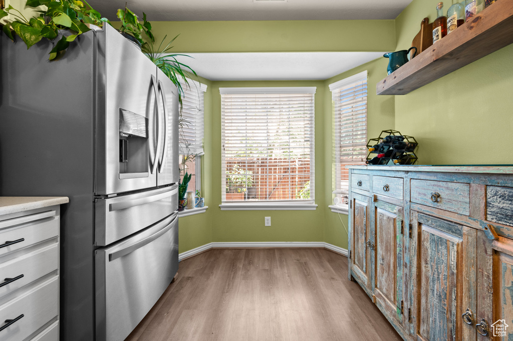 Kitchen with stainless steel fridge with ice dispenser, light wood-style flooring, light countertops, and open shelves