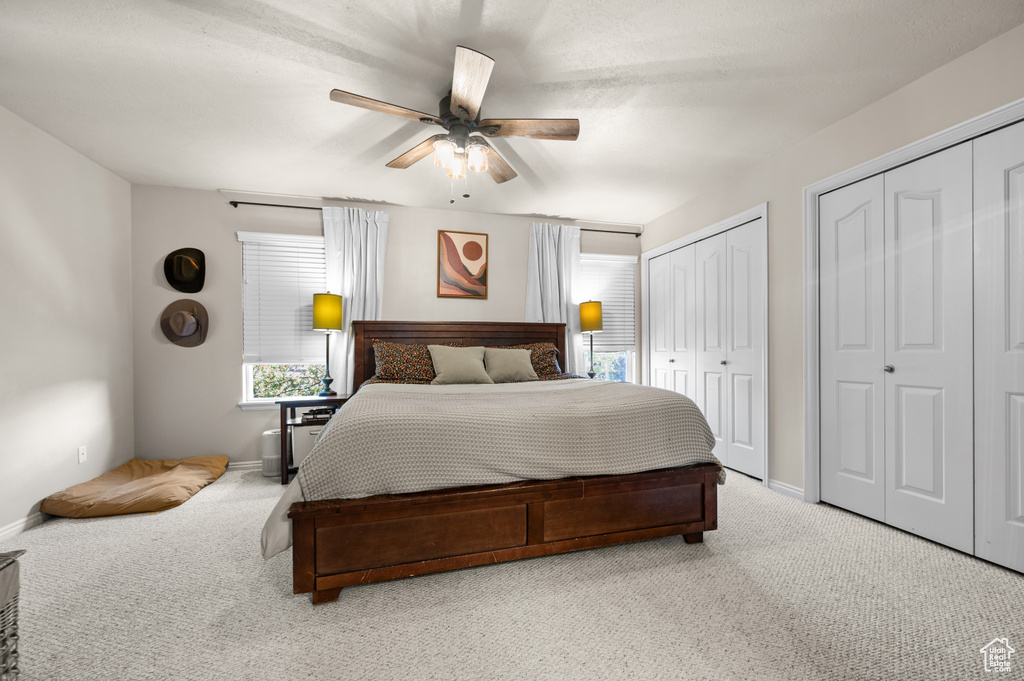 Bedroom with light colored carpet, multiple closets, and a ceiling fan
