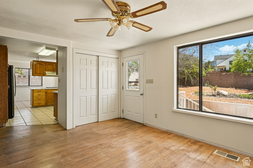 Unfurnished bedroom featuring freestanding refrigerator, light wood finished floors, ensuite bath, a closet, and a ceiling fan