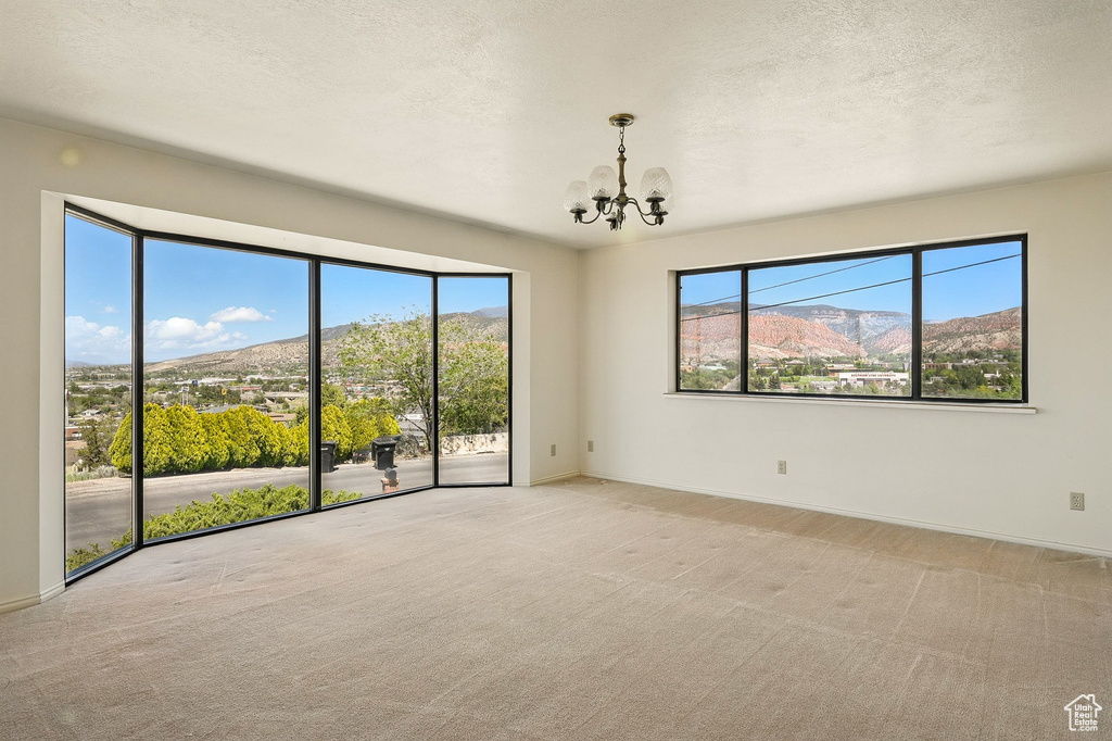 Spare room with a chandelier, carpet floors, a textured ceiling, and a mountain view