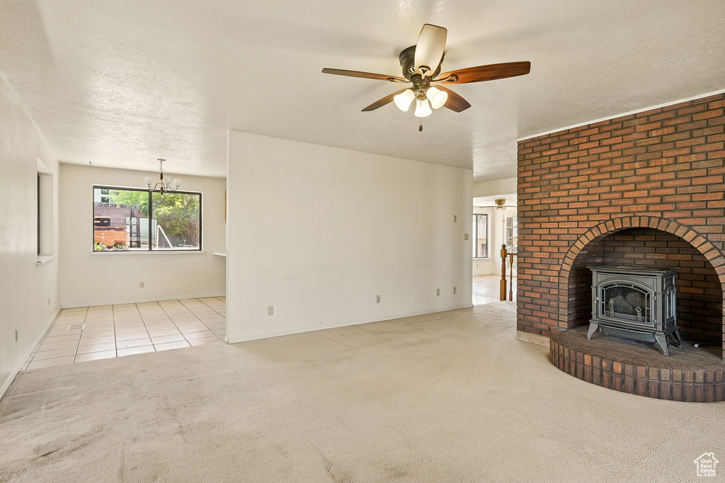 Unfurnished living room featuring a wood stove, carpet floors, ceiling fan, a chandelier, and a textured ceiling