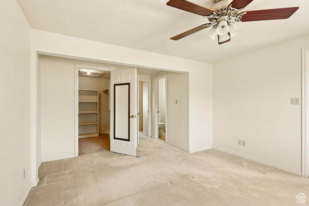 Unfurnished bedroom with light colored carpet, a walk in closet, a closet, a ceiling fan, and ensuite bath