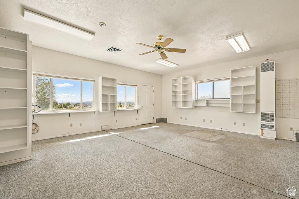 Carpeted spare room with a heating unit, a textured ceiling, and ceiling fan
