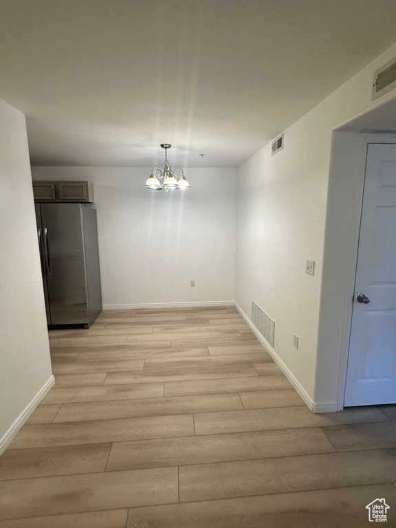 Unfurnished dining area featuring light wood-style flooring and a chandelier