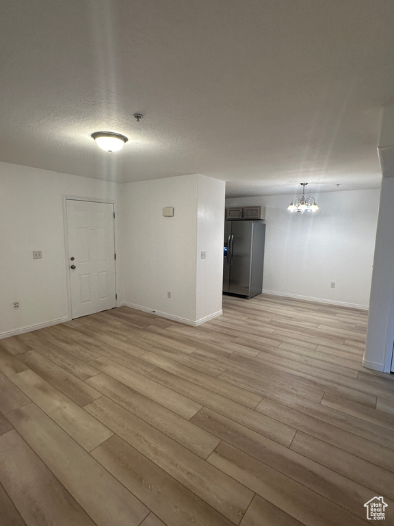 Spare room with light wood finished floors, a chandelier, and fire sprinkler in ceiling