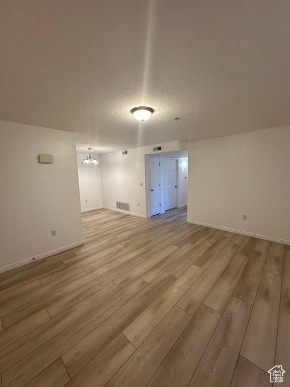Empty room featuring a chandelier, light wood-style flooring, and a textured ceiling