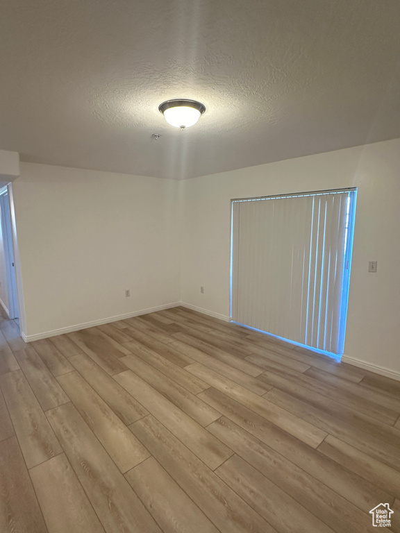 Empty room featuring light wood-type flooring and a textured ceiling