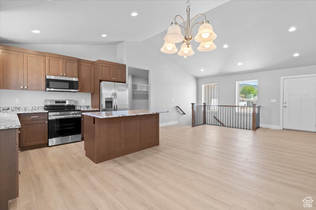 Kitchen featuring appliances with stainless steel finishes, lofted ceiling, a center island, light wood-style floors, and a chandelier