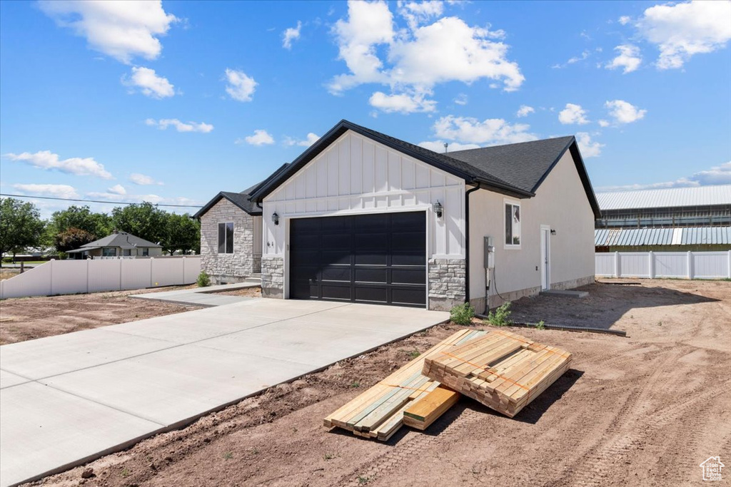 View of front of property with a garage, board and batten siding, driveway, and stone siding