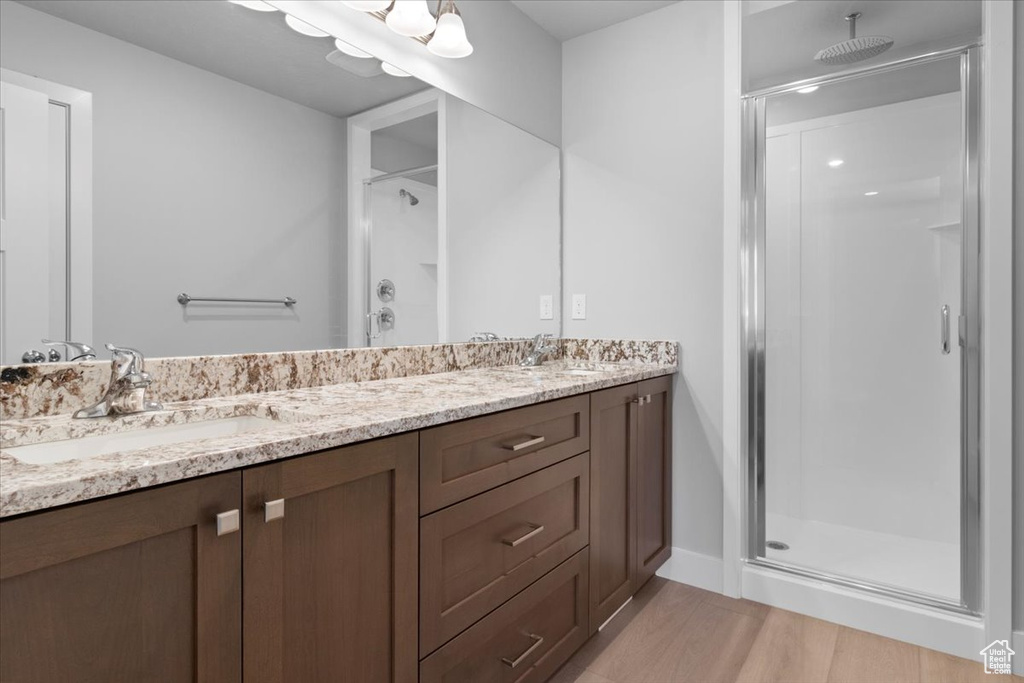 Full bath featuring a shower stall, double vanity, and wood finished floors