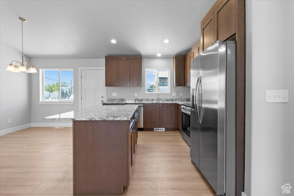 Kitchen with stainless steel appliances, light wood-style flooring, a chandelier, a center island, and pendant lighting