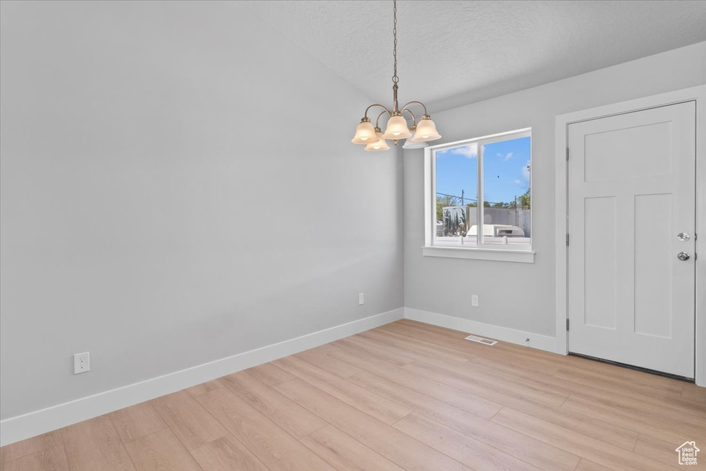 Unfurnished room featuring a chandelier, light wood-type flooring, a textured ceiling, and lofted ceiling