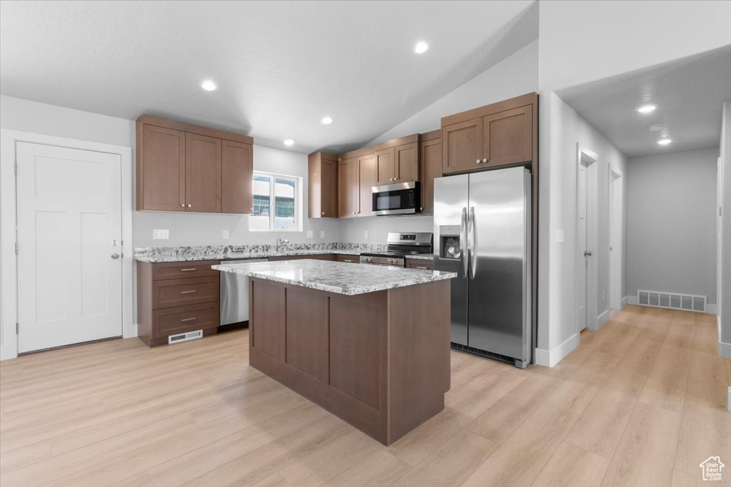 Kitchen featuring appliances with stainless steel finishes, light wood-style flooring, a kitchen island, light stone countertops, and lofted ceiling