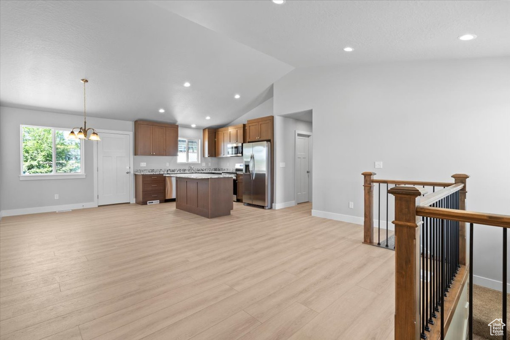 Kitchen with stainless steel appliances, a center island, light countertops, a chandelier, and lofted ceiling