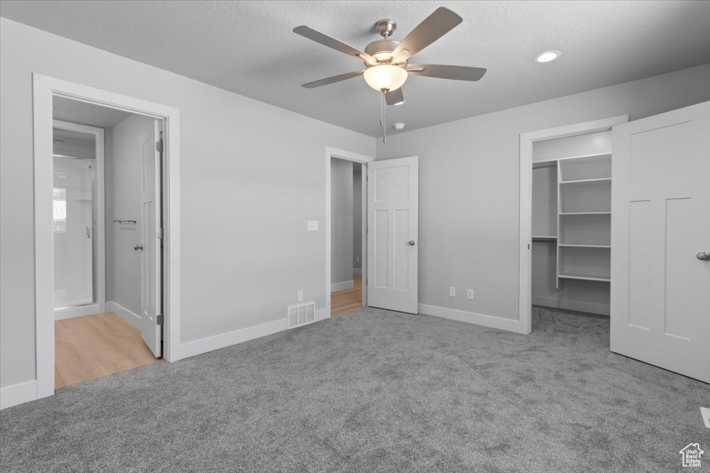 Unfurnished bedroom featuring carpet floors, a walk in closet, connected bathroom, a closet, and a ceiling fan
