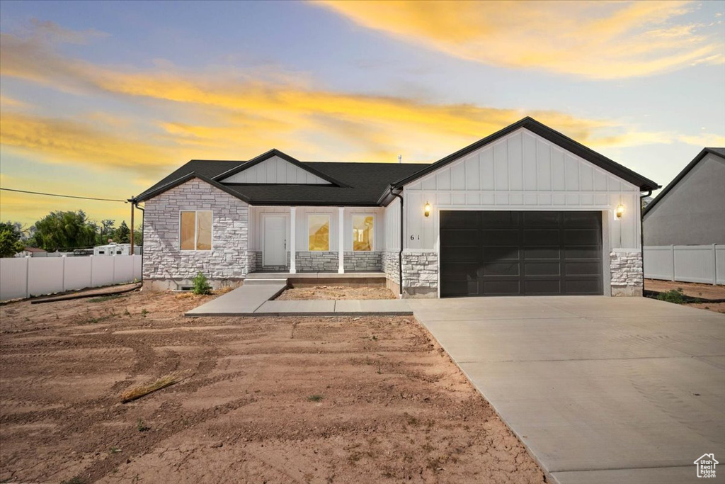 Modern inspired farmhouse featuring stone siding, an attached garage, board and batten siding, and driveway
