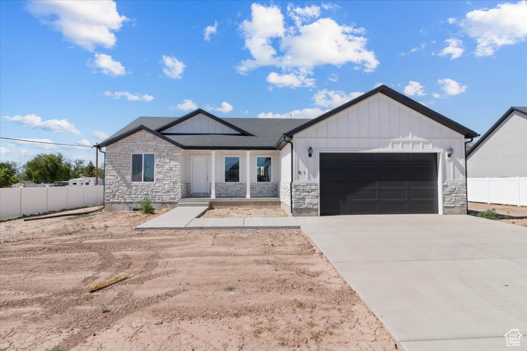 Modern inspired farmhouse featuring stone siding, an attached garage, board and batten siding, and concrete driveway