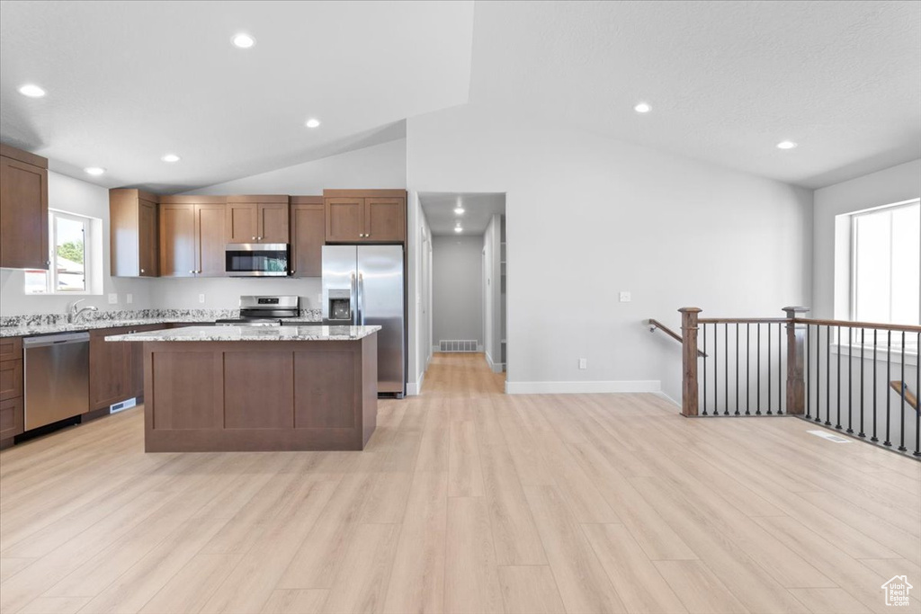 Kitchen featuring stainless steel appliances, vaulted ceiling, light wood finished floors, a kitchen island, and recessed lighting