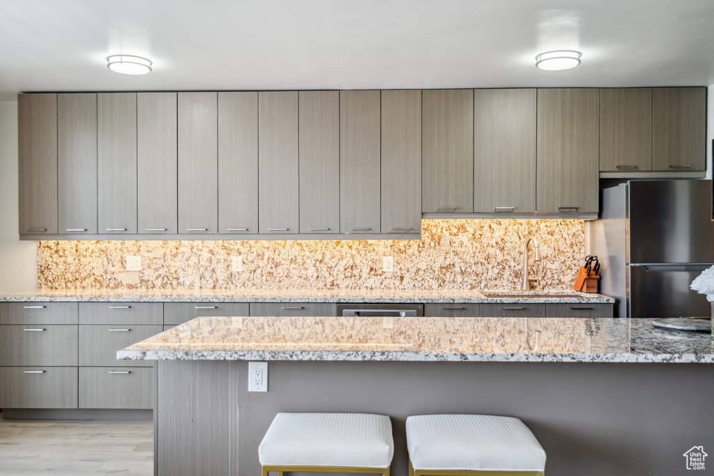 Kitchen featuring freestanding refrigerator, gray cabinetry, a kitchen breakfast bar, and backsplash