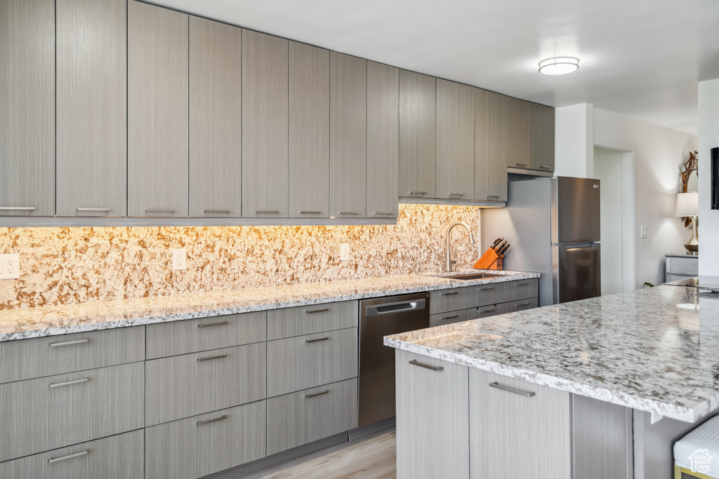 Kitchen featuring appliances with stainless steel finishes, gray cabinetry, light stone counters, light wood finished floors, and backsplash