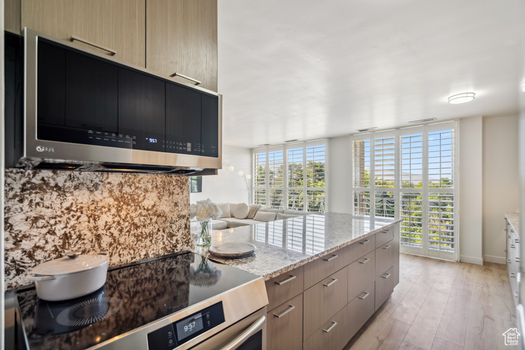 Kitchen with stainless steel microwave, stove, light stone counters, light wood finished floors, and modern cabinets