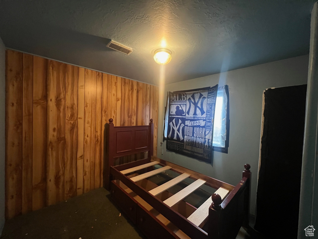 Carpeted bedroom featuring a textured ceiling and wooden walls
