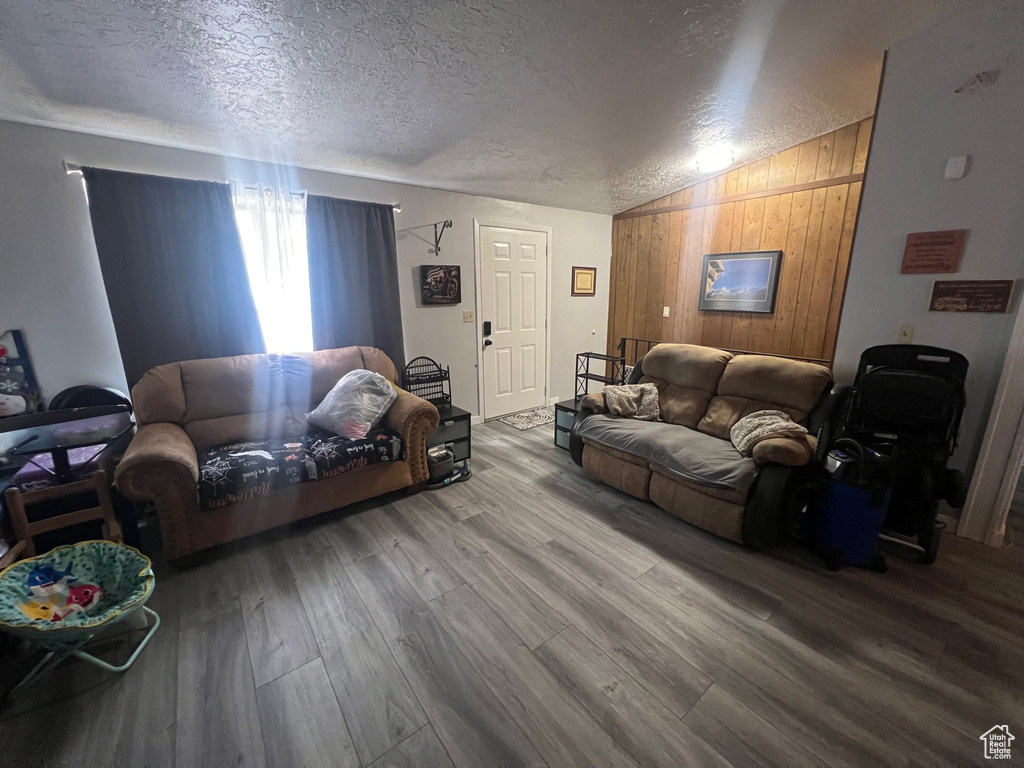Living room with vaulted ceiling, a textured ceiling, wood finished floors, and wooden walls