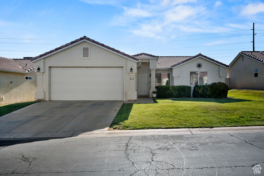 Ranch-style home featuring stucco siding, an attached garage, a tiled roof, a front yard, and concrete driveway