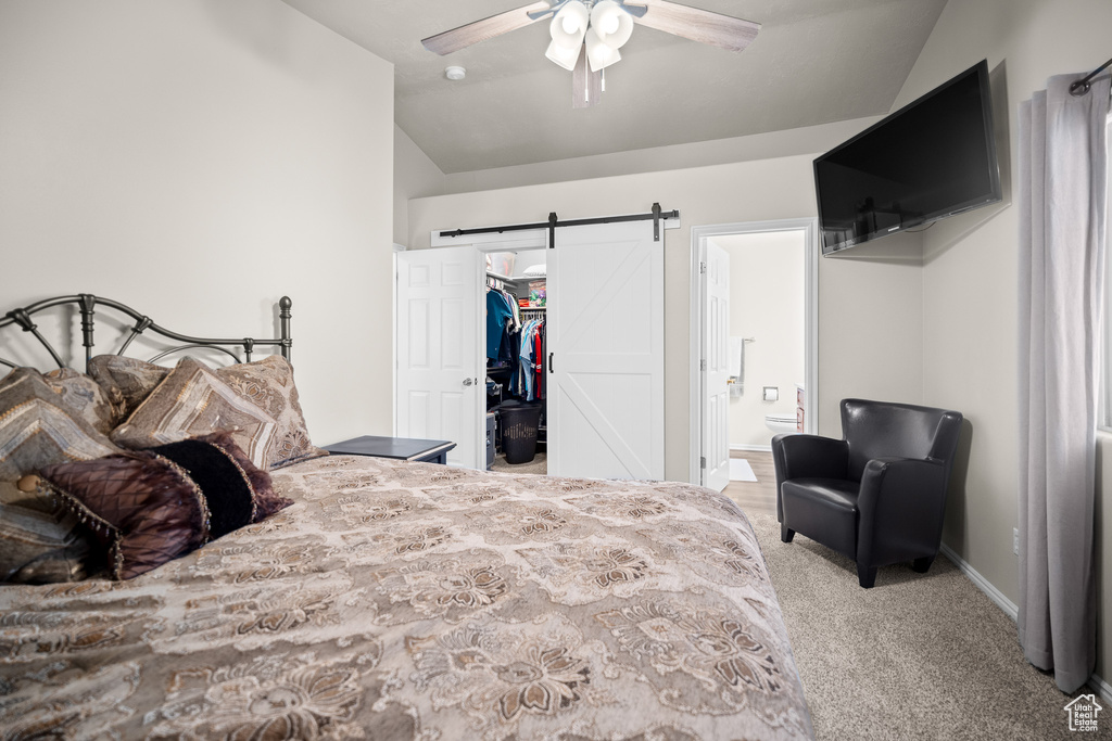 Carpeted bedroom with vaulted ceiling, a walk in closet, a barn door, ensuite bath, and a closet