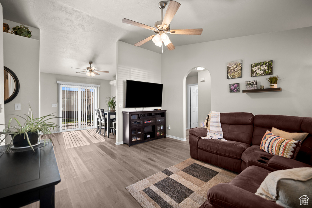 Living area featuring a ceiling fan, arched walkways, lofted ceiling, and wood finished floors