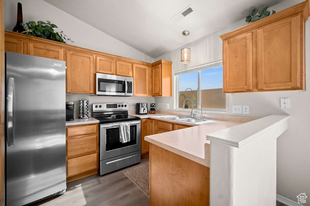 Kitchen with appliances with stainless steel finishes, a peninsula, vaulted ceiling, light countertops, and light wood-style flooring