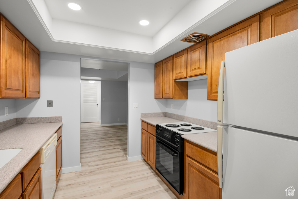 Kitchen with white appliances, light wood finished floors, light countertops, brown cabinets, and a raised ceiling