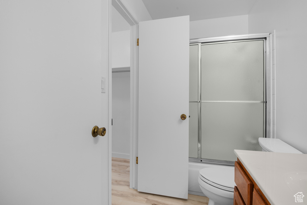 Full bathroom featuring wood finished floors, vanity, and bath / shower combo with glass door