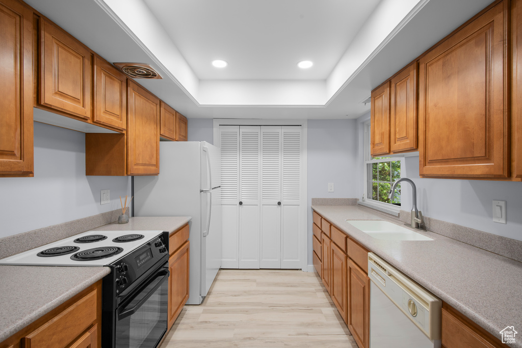 Kitchen with electric stove, white dishwasher, light wood-type flooring, brown cabinetry, and recessed lighting