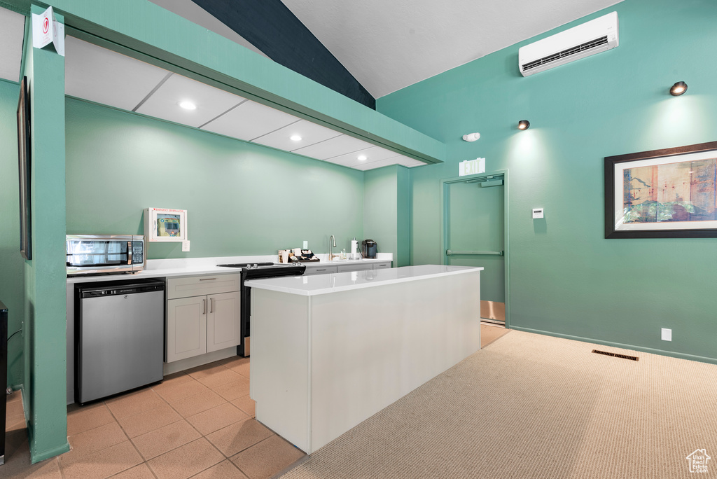 Kitchen featuring stainless steel appliances, an AC wall unit, light countertops, a kitchen island, and vaulted ceiling