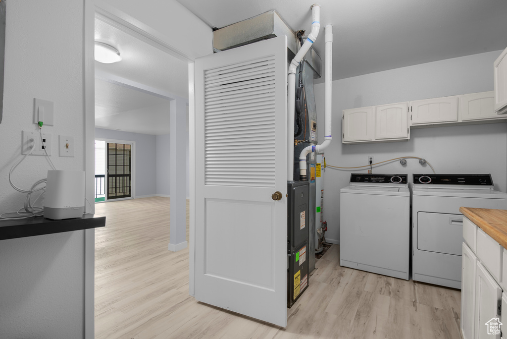 Laundry area featuring washing machine and clothes dryer, light wood-style floors, and cabinet space