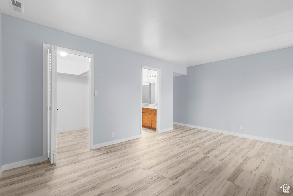 Unfurnished bedroom featuring light wood finished floors, a walk in closet, a closet, and ensuite bathroom