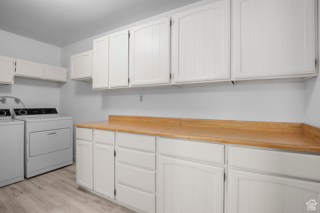 Laundry room featuring washing machine and clothes dryer, cabinet space, and light wood-type flooring