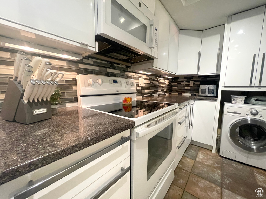 Kitchen with white appliances, washer / dryer, white cabinetry, and backsplash
