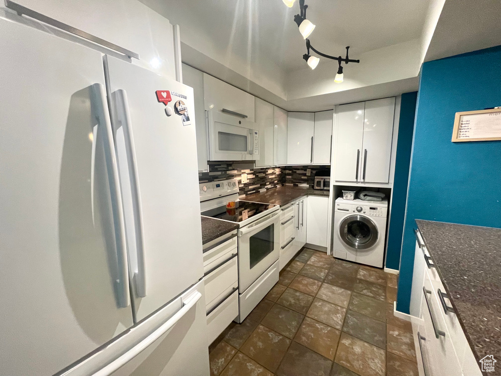Kitchen featuring white appliances, washer / dryer, white cabinets, backsplash, and stone finish flooring
